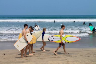 Kuta Beach, Bali, Endonezya arpı odaklı yürüyen sörfçüler, parlak tropikal ışık özgürlüğü, seyahat neşesini ve yaz yaşam tarzını gösteriyor. Turizm, tatil, sörf kültürü kavramları için ideal. 11 Eylül 2024.