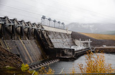 Yağmurlu bir günde devasa beton yapısı ve elektrik hatları olan endüstriyel hidroelektrik barajı. Mühendislik, enerji üretimi, sürdürülebilirlik ve yenilenebilir güç sembolü