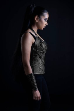 Şehir tarzı fantezi kostüm giyen ve siyah bir fonda duran çekici, koyu saçlı bir kadın.