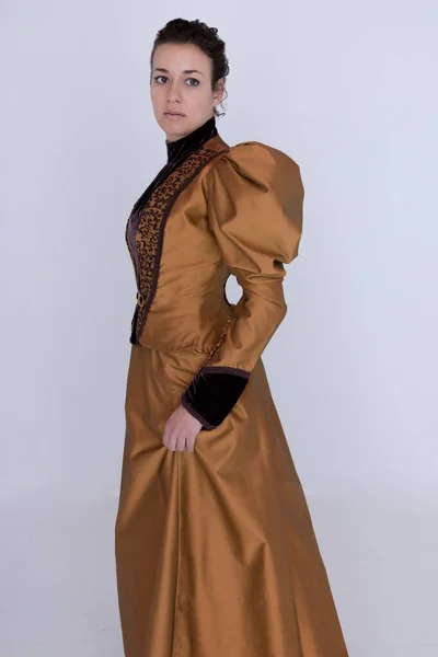 青銅と茶色の絹のアンサンブルを身に着けているビクトリア朝の女性と白い背景に立って — ストック写真