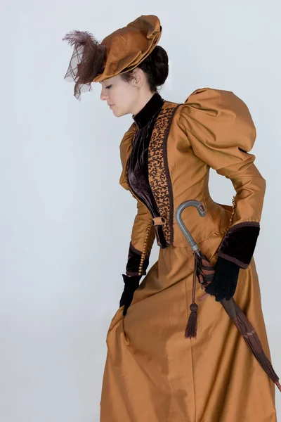 青銅と茶色の絹のアンサンブルを身に着けているビクトリア朝の女性と大きな帽子と白い背景の前でポーズ — ストック写真
