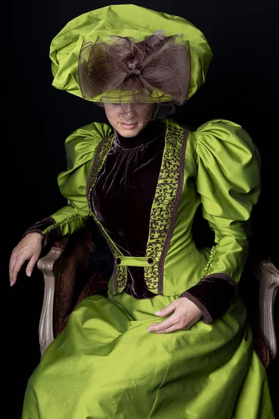 维多利亚时代的女人 穿着绿色和棕色的丝绸衣服 坐在华丽的红色天鹅绒椅子上 — 图库照片