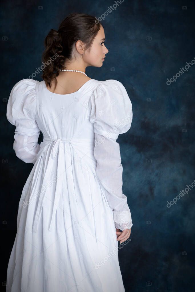 A young Regency woman standing alone against a blue backdrop