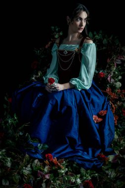 Rönesans ya da peri masalı kadın kırmızı ipek korse ve mavi ipek etek giyiyor ve sarmaşıklar ve çiçeklerle çevrili.