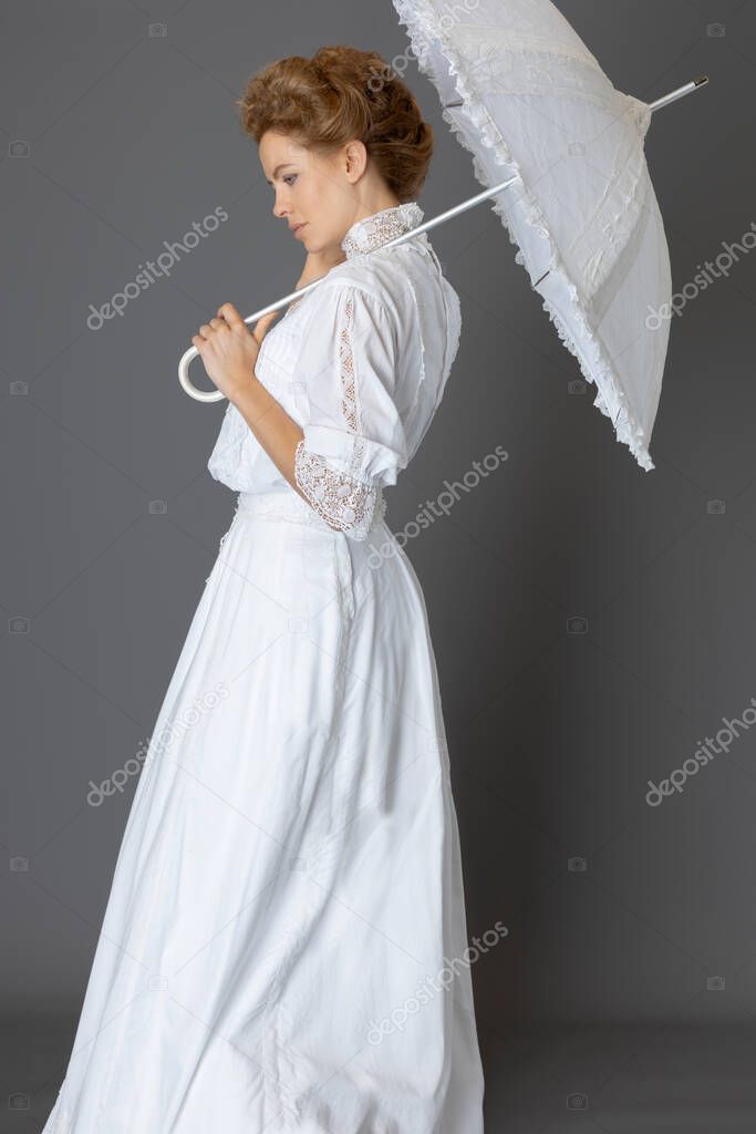 An Edwardian woman wearing a white lace blouse and skirt with a long pearl necklace and carrying a parasol