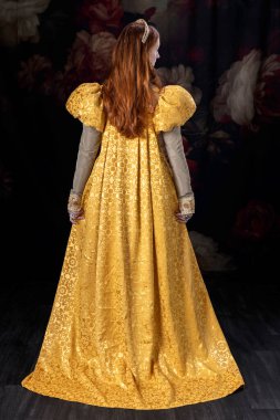 Kizil saçli bir kadin, Rönesans elbisesi giyiyor, kabarık kollu, tek basina duruyor.