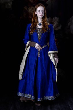 Mavi ve altın rengi bir elbise giyen kızıl saçlı bir kadın. 