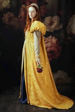 Kizil saçli bir kadin, Rönesans elbisesi giyiyor, kabarık kollu, tek basina duruyor.