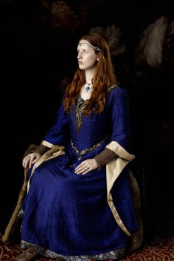 Mavi ve altın rengi bir elbise giyen kızıl saçlı bir kadın. 