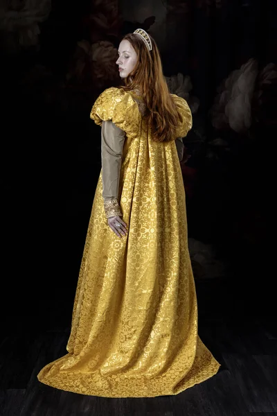 Kizil saçli bir kadin, Rönesans elbisesi giyiyor, kabarık kollu, tek basina duruyor.