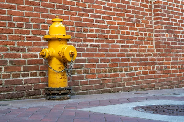 Ein Gelber Feuerhydrant Gegen Eine Rote Backsteinmauer — Stockfoto