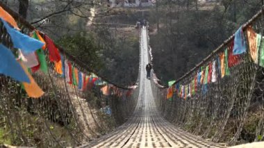 Derin bir vadide sallanan bir köprüden sarkan bayraklar.