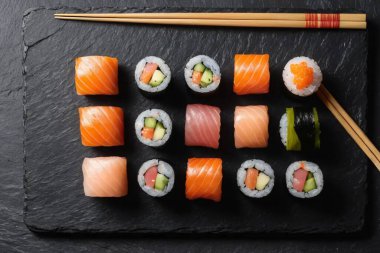 Güzel hazırlanmış somon suşisi ve siyah tahtada rulo. Yanında da yemek çubukları, enfes bir Japon yemeği deneyimi..