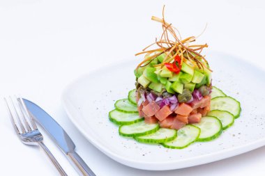 Avokado, salatalık, kapari ve kırmızı soğanlı alabalık tartar. Kızarmış pırasa ve kırmızı biberle süslenmiş. Yakın plan, beyaz arkaplan.