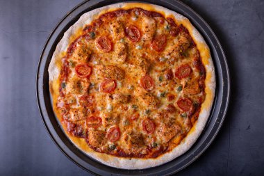 Somonlu pizza, domates ve kapari. Pizzanın tamamı siyah arka planda. Yakın çekim, üst görünüm.