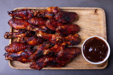 Ahşap bir tahtanın üzerinde ızgara soslu kızarmış tavuk kanadı. Siyah arkaplan, yakın plan.