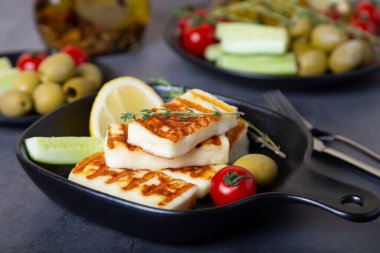 Siyah tavada ızgara haloumi peyniri, zeytin, domates, salatalık ve biberli. Yakın plan..