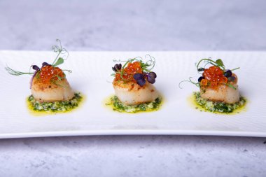 Havyarlı deniz tarakları, mikroyeşiller ve beyaz tabakta yeşil sos. Yakın plan..