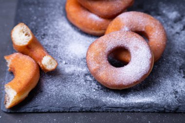 Pudra şekerli çörekler. Geleneksel donutlar, siyah arka planda yağda kızartılmış halka şeklinde. Abur cubur. Yakın plan..