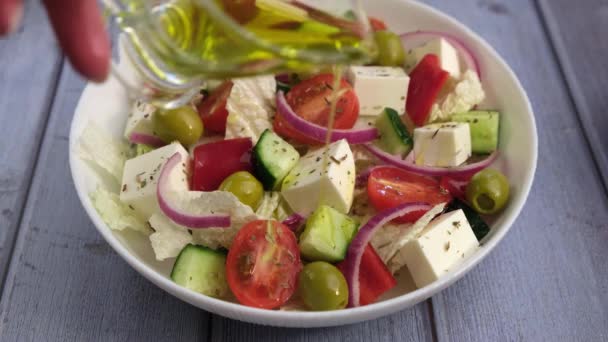 ギリシャのサラダにオリーブオイルを入れます 伝統的なギリシャ料理 健康的なベジタリアン料理 白皿に新鮮な野菜やフェタチーズ — ストック動画