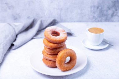 Pudra şekerli çörekler ve bir fincan kahve. Yağ içinde kızartılmış halka şeklinde geleneksel çörekler. Sağlıksız ama lezzetli yiyecekler. Yakın plan, hafif arkaplan.