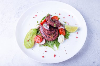 Ahtapot salatası, kiraz domatesleri, avokado, roka, bıldırcın yumurtası, turp ve beyaz tabakta limon. Geleneksel Akdeniz yemeği. Yakın plan, beyaz arkaplan.