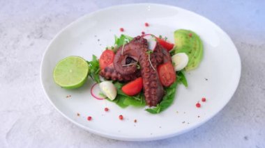 Ahtapot salatası, kiraz domatesleri, avokado, roka, bıldırcın yumurtası, turp ve beyaz tabakta limon. Geleneksel Akdeniz yemeği. Yakın plan, beyaz arkaplan, kamera yakınlaştırması.