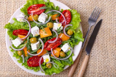 Balkabaklı, peynirli sıcak salata, güneşte kurutulmuş domates, zeytin, roka ve kırmızı soğan. Yakın plan..