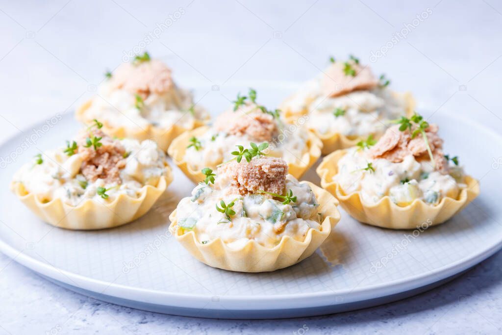 Tartlets stuffed with codfish liver, codfish caviar, cucumber and microgreens. Traditional cold portioned appetizer in a pastry basket. Close-up.