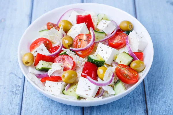 Greek salad. Traditional Greek dish. Healthy vegetarian food. Fresh vegetables and feta cheese in a white plate. Close-up, blue background.