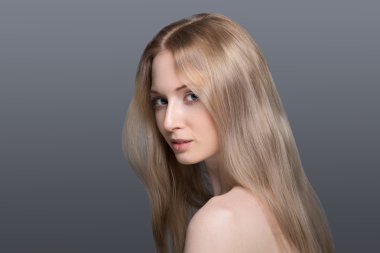 Onun yeteneklerine emin. Genç sarışın kadın tutuşup kalça üzerinde gülümseyen ve gri arka plan karşı dururken kamera bakıyor