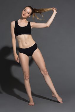 Güzelliğine güveniyor. Siyah iç çamaşırı çekici genç kadın poz ve gri arka plan karşı dururken kameraya bakıyor