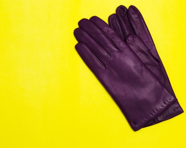 woman violet leather gloves on yellow background top view flat lay