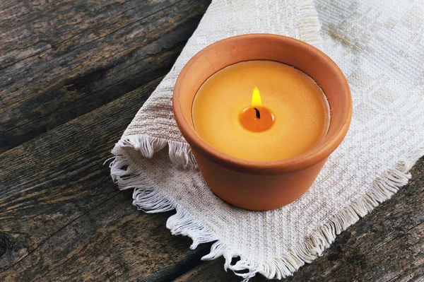 Ahşap arka plan üzerinde toprak kap içinde yanan mum
