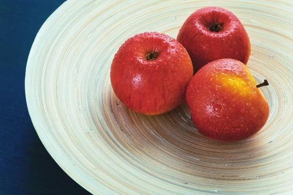 Red apples on a wooden plate on a blue background — Stock Photo, Image