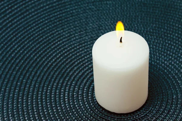 Burning white candle on a blue background