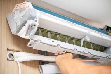 Duvara monte edilmiş beyaz bir klimayı ahşap panelli bir odanın içinde kuran veya onaran bir elin yakın çekim görüntüsü..