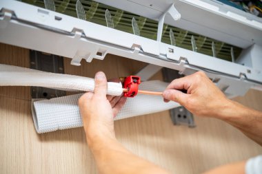 Bir kişi, ev ortamında kırmızı bir kıskaçla duvarlara monte edilmiş bir klimaya bakır bir boru yerleştirir ve emniyete alır..