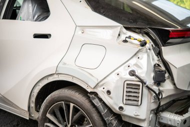 Arka paneli sökülmüş beyaz bir araba ve bir kaportacı dükkanında tamir ediliyor..