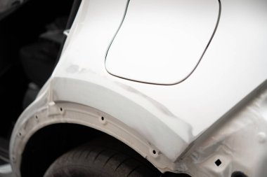 Bir araç tamirhanesinin arka tekerine astar takılmış beyaz bir araba çamurluğunun yakın çekim görüntüsü..