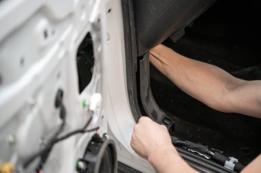 Bir tamircinin elleri kaportacının içindeki beyaz bir arabanın iç kapısında çalışıyor..