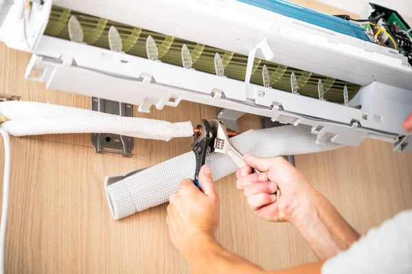 Duvara monte edilmiş havalandırma sisteminin bakır borularını tamir etmek için anahtarlar kullanan eller..