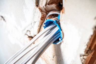 İnşaat sırasında kısmen sıvanmış bir duvara gömülü mavi plastik bir kanaldan çıkan çoklu beyaz elektrik kablolarının yakın çekimi.