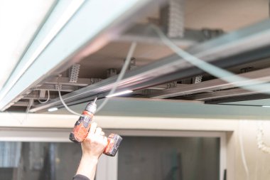 Elektrik matkabıyla el, modern iç mekanda askıya alınmış tavan iskeletine LED ray ışıklandırması yükler.