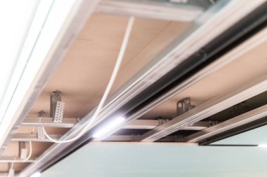 Çağdaş bir iç mekanda LED ray aydınlatma ve metal destekleri içeren askıya alınmış tavan iskeletinin kapatılması.