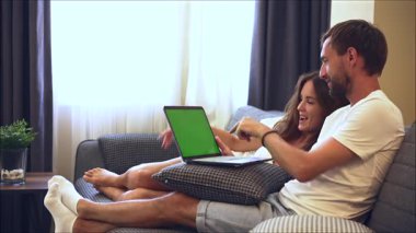 Çift kanepede dinlenirken yeşil ekranlı dizüstü bilgisayar kullanıyor