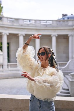 Paris 'te güneş ışığında dans eden şık bir kadın fırfırlı bluz giyiyor.