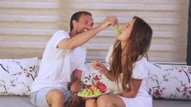 Gülümseyen çift rahat koltukta üzüm paylaşıyor.