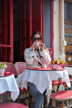 Trençkotlu kadın Paris caddesindeki kafede kahve içiyor.