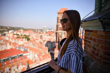 Güneş gözlüklü turist kadın, tarihi Gdansk Eski Kasabası 'nın çatı katındaki Polonya manzarasının keyfini çıkarıyor.